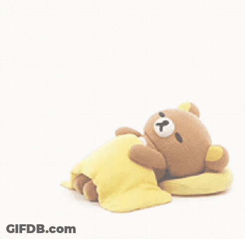 A Teddy Bear Is Laying On A Yellow Blanket Next To A Pillow . GIF