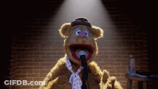 A Teddy Bear Is Singing Into A Microphone While Wearing A Tie . GIF