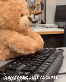 A Teddy Bear Is Sitting At A Desk Typing On A Computer Keyboard . GIF