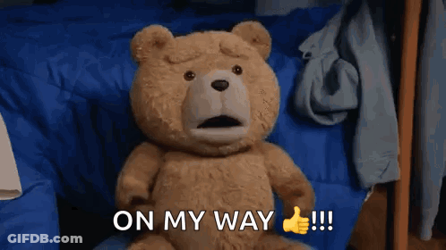 A Teddy Bear Is Sitting On A Bed And Giving A Thumbs Up Sign GIF