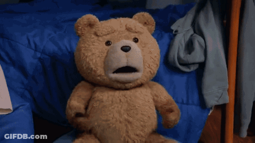A Teddy Bear Is Sitting On A Bed With Its Mouth Open GIF