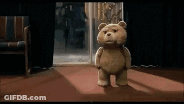 A Teddy Bear Is Standing In Front Of A Door In A Room GIF