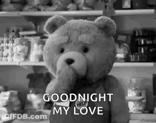 A Teddy Bear Is Standing In Front Of A Refrigerator And Holding Its Hand To Its Mouth . GIF