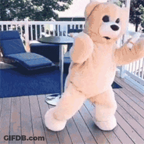 A Teddy Bear Is Standing On A Deck With A Table And Chairs In The Background GIF