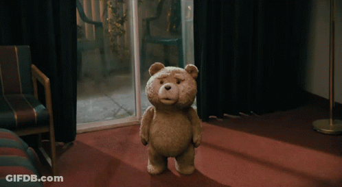 A Teddy Bear Is Standing On A Red Carpet In A Dark Room GIF