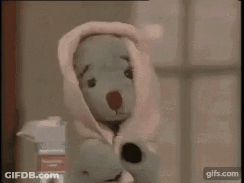 A Teddy Bear Is Wrapped In A Pink Blanket And Standing Next To A Window . GIF