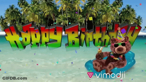 A Teddy Bear Sitting On A Beach With The Words Happy Birthday Behind Him GIF