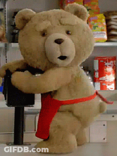 A Teddy Bear Wearing A Red Apron Is Standing On A Counter In A Store GIF