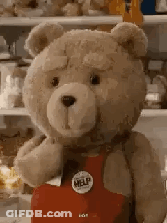 A Teddy Bear Wearing A Red Apron With A Help Button On It Is Standing In Front Of A Refrigerator . GIF