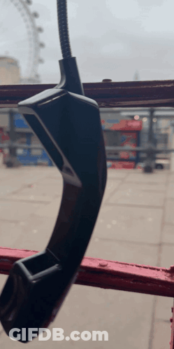A Telephone Hanging From A Red Railing With A Ferris Wheel In The Background GIF