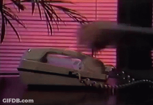 A Telephone Is On A Table In Front Of A Window With Blinds . GIF