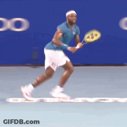 A Tennis Player In A Blue Shirt And White Shorts Holds A Wilson Racquet GIF