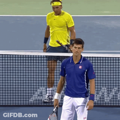 A Tennis Player In A Blue Shirt Stands Next To A Player In A Yellow Shirt On A Tennis Court GIF