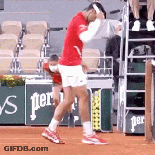 A Tennis Player In A Red Shirt And White Shorts Is Dancing On A Tennis Court . GIF
