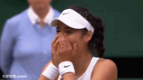 A Tennis Player Is Covering Her Face With Her Hands While Wearing A White Hat And Wristbands . GIF