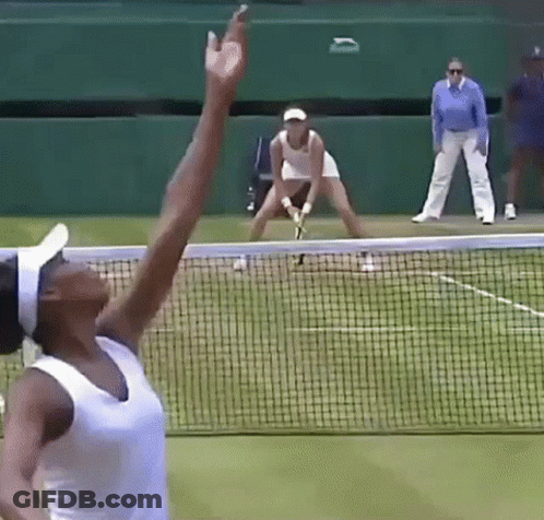 A Tennis Player Is Reaching For The Ball While Another Player Stands Behind Her GIF