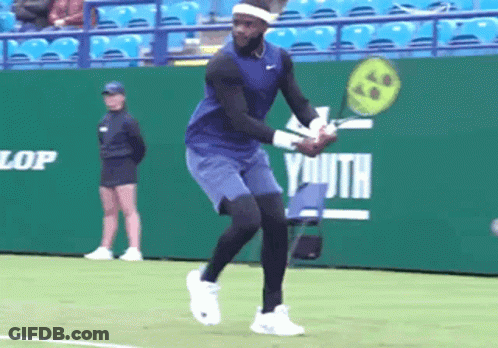 A Tennis Player Is Swinging A Racket In Front Of A Green Wall That Says Dunlop Youth GIF