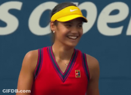 A Tennis Player Wearing A Red Tank Top And A Yellow Visor Is Smiling On A Tennis Court . GIF