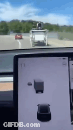 A Tesla Model 3 Is Driving Down A Highway Next To A Truck And A Red Car . GIF
