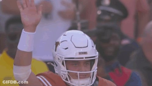 A Texas Football Player Wearing A White Helmet Holds His Hand Up GIF