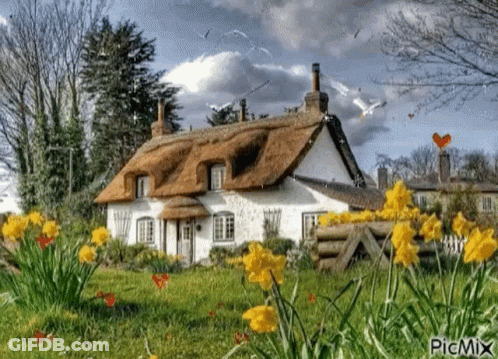 A Thatched Roofed Cottage With Flowers In Front Of It GIF
