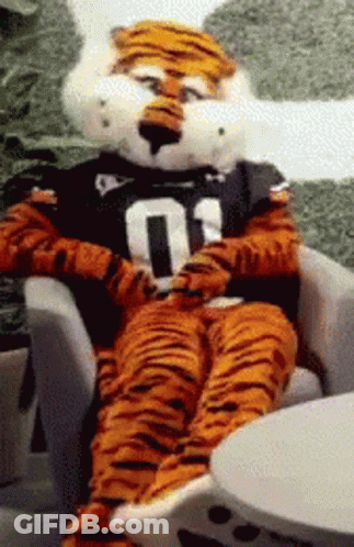 A Tiger Mascot Is Sitting In A Chair Wearing A Number 01 Shirt GIF