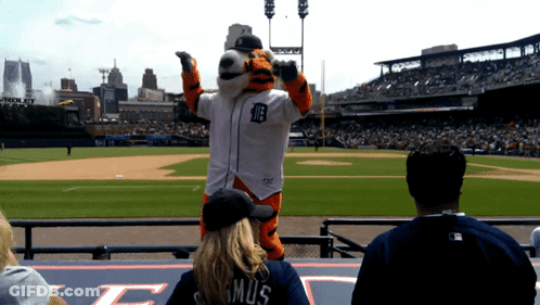 A Tiger Mascot Stands On A Baseball Field With A Woman Wearing A Shirt That Says Mus GIF