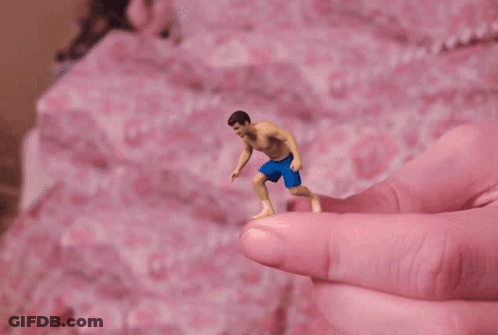 A Tiny Figure Of A Man In Blue Shorts Is Being Held By A Pink Finger GIF