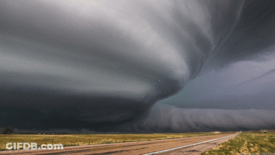 A Tornado Is Moving Over A Dirt Road In The Middle Of A Field GIF