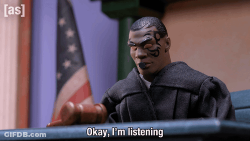 A Toy Judge Says " Okay I 'M Listening " In Front Of A Flag GIF
