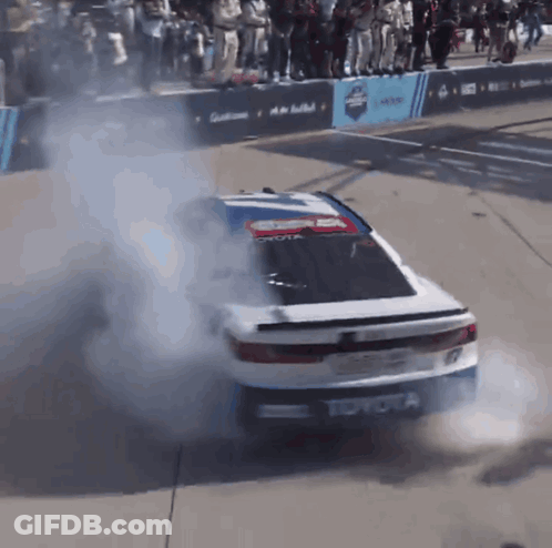 A Toyota Race Car Is Doing A Burnout In Front Of A Crowd GIF