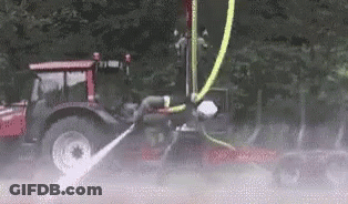 A Tractor With A Hose Attached To It Is Spraying Water On A Car . GIF