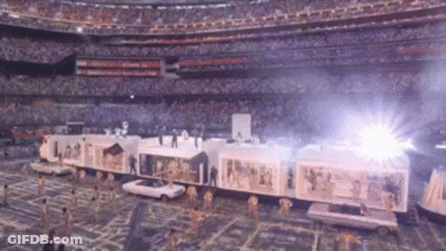 A Train Is Being Pulled By Cars In A Stadium With A Crowd In The Background GIF