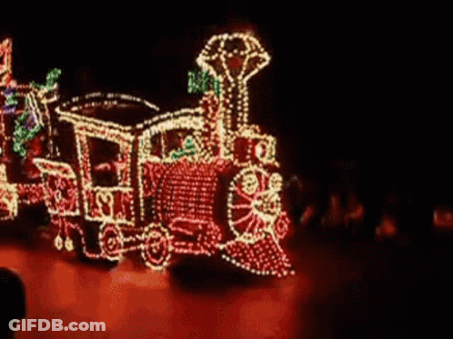 A Train Is Decorated With Christmas Lights And Is Driving Down A Street . GIF