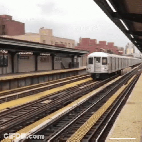 A Train Is Going Down The Tracks At A Station With A Building In The Background GIF