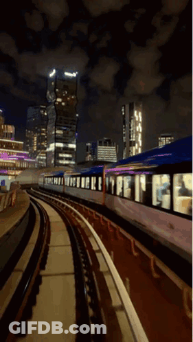 A Train Is Going Down The Tracks At Night With Buildings In The Background GIF