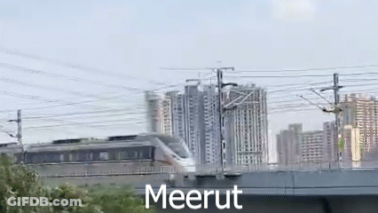 A Train Is Going Over A Bridge In Front Of A Building . GIF