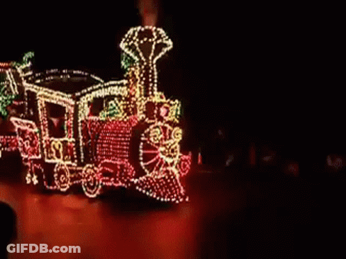 A Train With Christmas Lights On It Is Driving Down A Street GIF