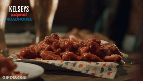 A Tray Of Chicken Wings Sits On A Table With A Sign That Says Kelseys Original Roadhouse GIF