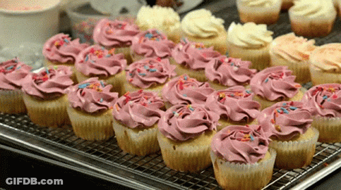 A Tray Of Cupcakes With Pink Frosting And Sprinkles On Them GIF