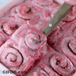 A Tray Of Pink Cinnamon Rolls With A Knife In It . GIF