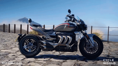 A Triumph Motorcycle Is Parked In Front Of A Mountain GIF