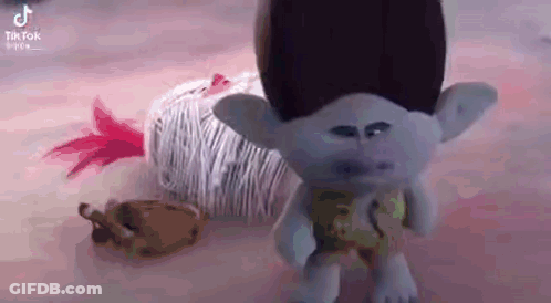 A Troll Doll Is Standing Next To A Ball Of Yarn On A Table . GIF