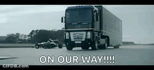 A Truck Is Driving Down A Road Next To A Race Car With The Words `` On Our Way !!! '' Written On It . GIF