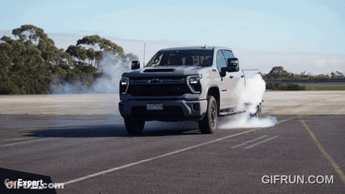 A Truck With Smoke Coming Out Of The Tires Is Driving Down A Road With A Car Expert Logo In The Corner GIF