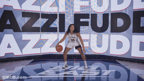 A Uconn Basketball Player Dribbles A Ball In Front Of A Large Screen That Says Azzi Fudd GIF