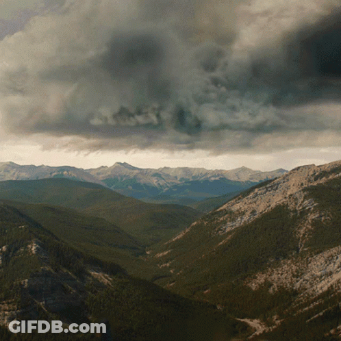 A Valley With Mountains In The Background And A Cloudy Sky In The Background GIF