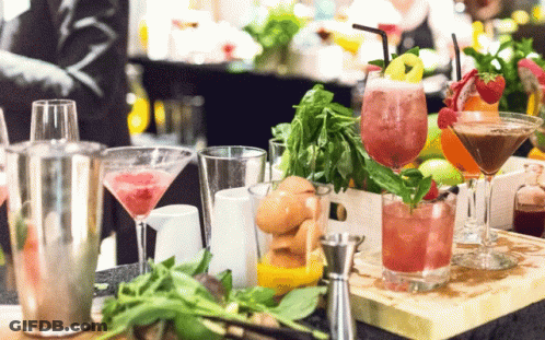 A Variety Of Drinks Are On A Table Including A Martini With Strawberries GIF
