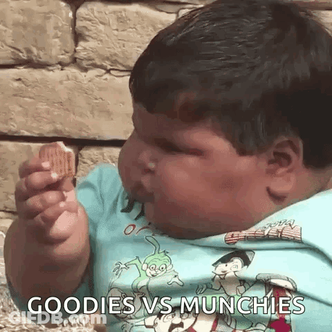 A Very Fat Boy Is Eating A Cookie With The Words Goodies Vs Munchies Written On His Shirt . GIF