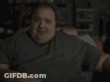 A Very Fat Man Is Sitting On A Couch In A Dark Room . GIF